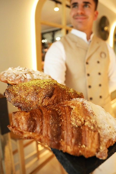 Hombre joven muestra tres cruasanes rellenos gigantes de diferentes sabores